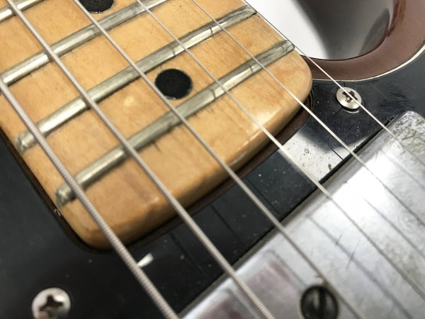 Close-up of electric guitar fretboard with strings and pickups showing worn wood and metal frets