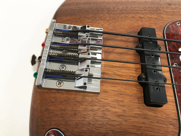 Close-up of Coffee House Guitars electric bass guitar bridge and pickup on natural wood body with four black strings and color-coded string ends
