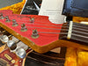 Close-up of red Fender guitar headstock with six tuning pegs, metal strings, and partial view of yellow guitar case with Certificate of Authenticity from Coffee House Guitars in the background