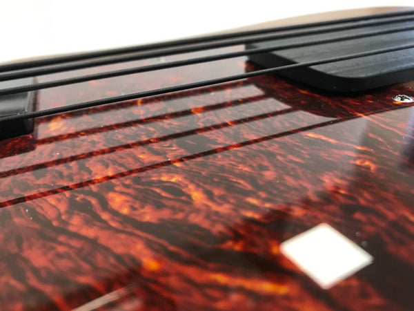 Close-up of tortoiseshell pickguard and black bass guitar strings on electric bass guitar body with glossy finish