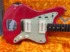 Vintage red Fender Jazzmaster electric guitar with white pickups and control knobs on orange plush case interior