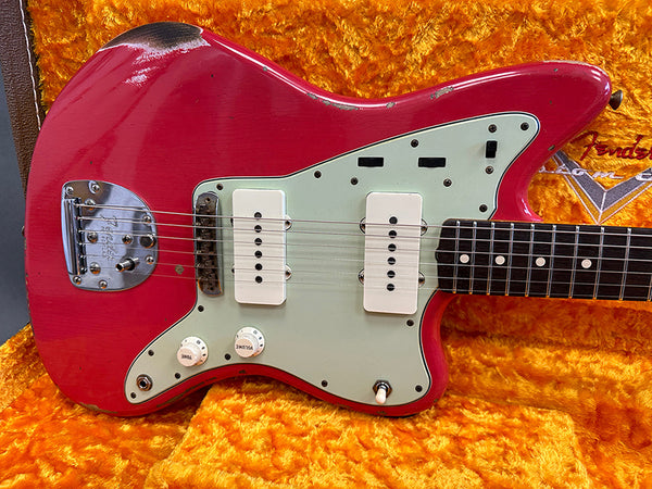 Vintage red Fender Jazzmaster electric guitar with white pickups and control knobs on orange plush case interior