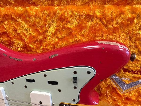 Close-up of vintage red electric guitar body with white pickguard and black switches on orange plush background