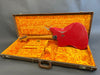 Vintage red Fender electric guitar shown from the back in an open brown hardshell case with bright orange plush interior lining and Fender logo embossed inside the lid.