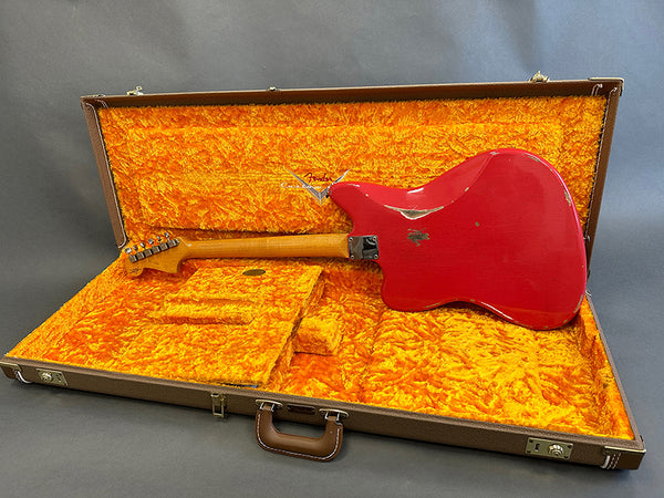 Vintage red Fender electric guitar shown from the back in an open brown hardshell case with bright orange plush interior lining and Fender logo embossed inside the lid.
