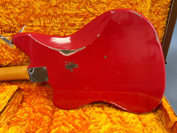 Red vintage electric guitar body with visible wear and scratches, resting on orange plush guitar case interior.