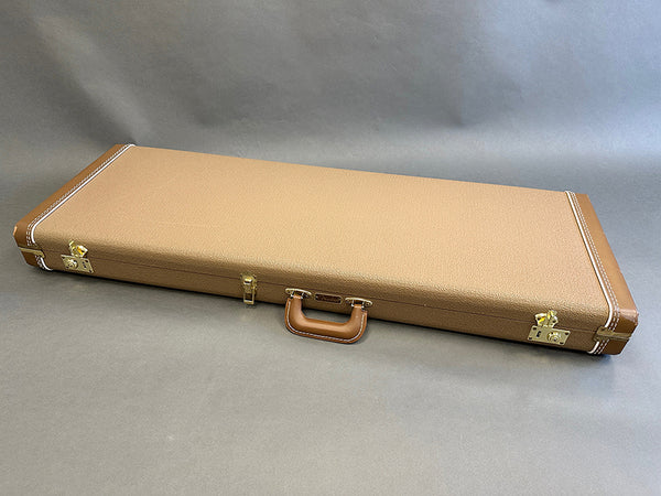 Brown textured hard guitar case with leather handle and gold metal clasps on gray background