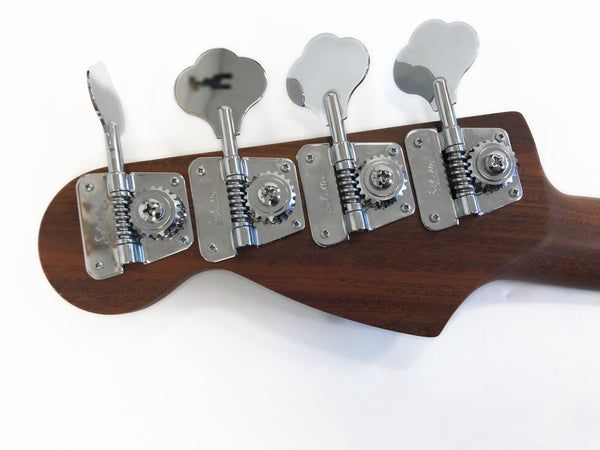 Close-up of bass guitar headstock showing four chrome tuning pegs and wooden finish against white background