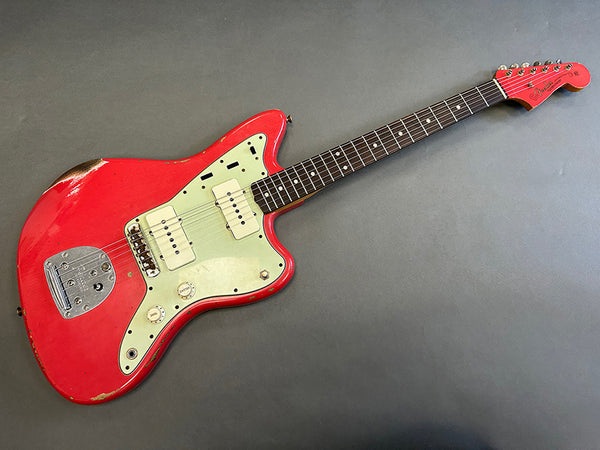 Vintage red electric guitar with cream pickguard and rosewood fretboard, showing worn finish and dual pickups, displayed on gray background.