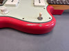 Close-up of red electric guitar body with wear and paint chips, white volume knob, pickup switch, and cream pickguard on gray surface.