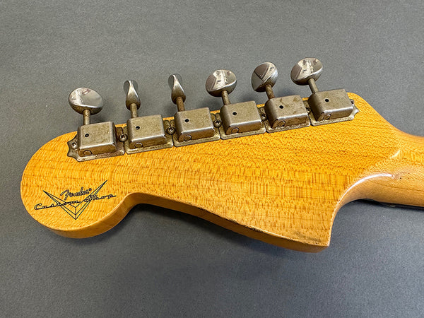 Close-up of vintage Fender Custom Shop guitar headstock with six metal tuning pegs on a textured wood finish background