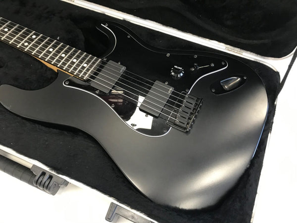 Black electric guitar with dual EMG pickups and volume knob, resting in a black padded hard case