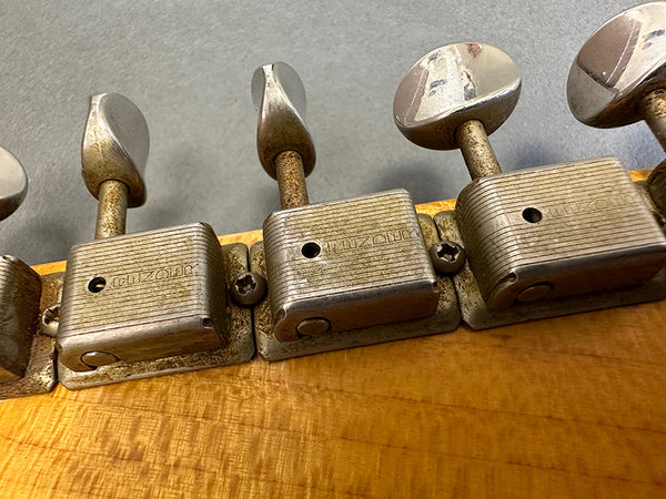 Close-up of vintage Kluson guitar tuning pegs on wooden headstock showing worn metal tuning keys and screws