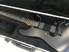 Matte black electric guitar with dual humbucker pickups, black pickguard, and volume control knob inside black plush-lined hard case, close-up of fretboard and body.