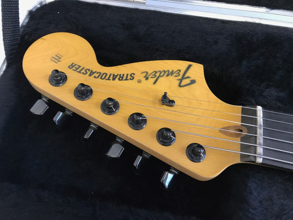 Close-up of Fender Stratocaster electric guitar headstock with tuning pegs and strings in black plush case