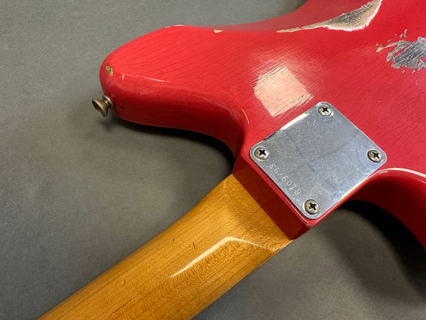 Vintage red electric guitar body with natural wood neck and metal neck plate on gray surface, close-up of worn finish and screws