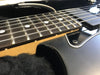 Close-up of black electric guitar fretboard with metal frets and white dot inlays on natural wood neck in soft black padded guitar case