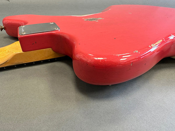 Close-up of red electric guitar body with worn finish and maple neck on gray background showing back plate and aging details