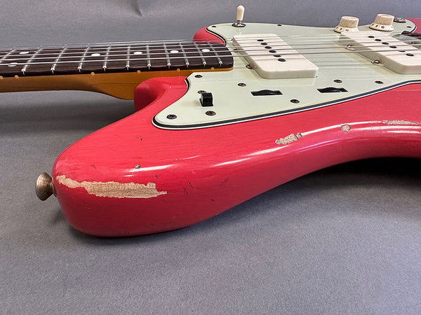 Close-up of red electric guitar body with white pickguard and visible wear and paint chips on grey background