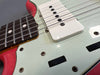 Close-up of electric guitar strings, white single-coil pickup, and black control knobs on red and white guitar body with rosewood fretboard and dot inlays.