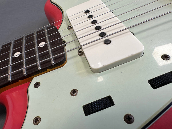 Close-up of electric guitar strings, white single-coil pickup, and black control knobs on red and white guitar body with rosewood fretboard and dot inlays.