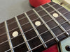 Close-up of electric guitar rosewood fretboard with metal frets and white dot inlays, showing six strings and part of red guitar body.