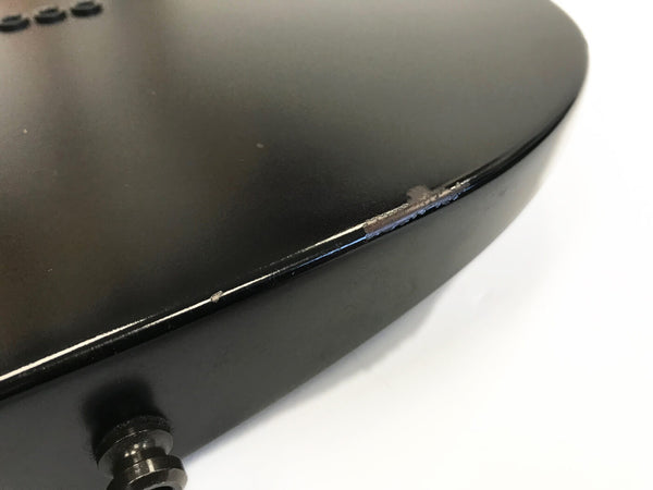 Close-up of black electric guitar body with visible chips and wear on the finish edge near the strap button.