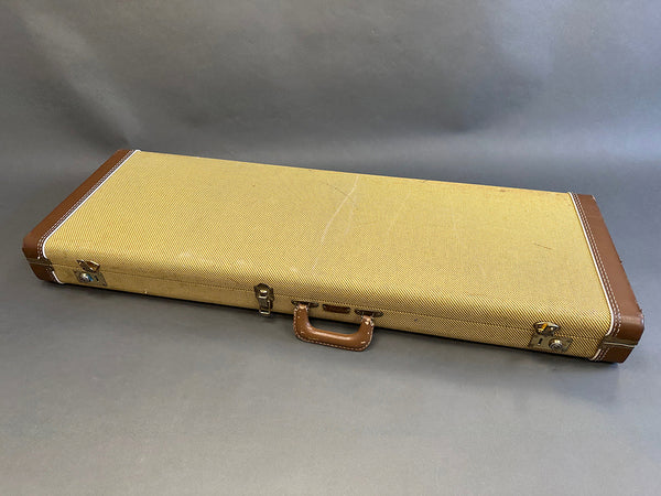 Vintage tweed hard guitar case with brown leather handle and corner reinforcements on gray background