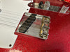 Close-up of red electric guitar body with white pickguard, metal bridge with Fender patent marking, and chrome control knobs.