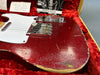 Close-up of a red 1958 Fender Telecaster electric guitar with worn and relic finish, white pickguard, chrome bridge and control knobs, resting in a red velvet-lined guitar case with owner's manual and notes in the background.