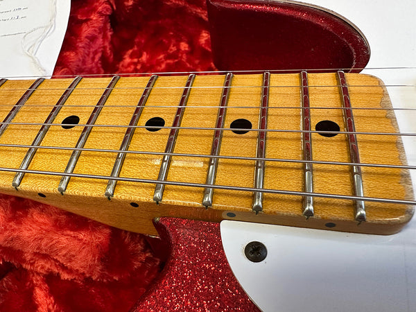 Close-up of vintage maple guitar neck and fretboard with metal frets and strings, red sparkle guitar body and white pickguard in background on plush red fabric case lining