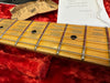Close-up of maple guitar neck with metal frets and black dot inlays resting on red plush fabric, showing guitar strings and part of a certificate and paper packaging from Coffee House Guitars.