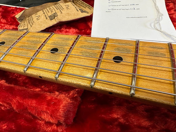 Close-up of maple guitar neck with metal frets and black dot inlays resting on red plush fabric, showing guitar strings and part of a certificate and paper packaging from Coffee House Guitars.