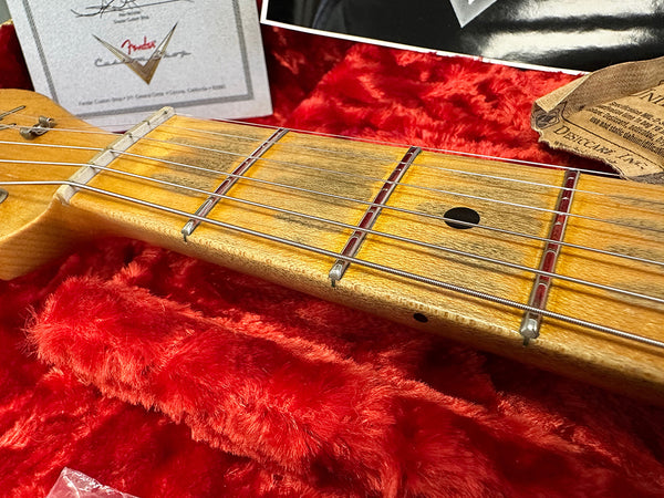 Close-up of vintage Fender guitar maple neck and frets on red plush case lining with certificate and desiccant packet in background