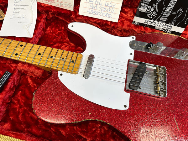 Close-up of vintage Fender Telecaster electric guitar in red sparkle finish with white pickguard and maple neck, displayed in red plush guitar case with owner's manual and Fender papers