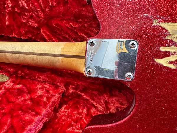 Close-up of maple neck joint plate with serial number on red sparkle finished electric guitar body in red plush case interior