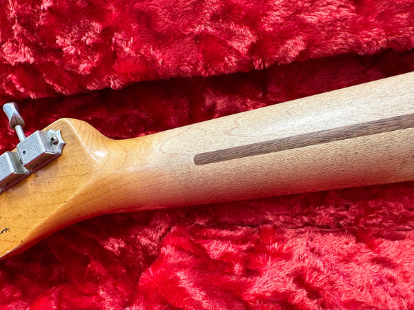 Close-up of guitar neck back with visible wood grain and metal tuning machine on red plush fabric background