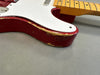 Close-up of red electric guitar body with white pickguard and visible wear and paint chipping on edges, showing vintage relic finish and maple neck with frets on gray background