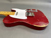 Close-up of vintage red electric guitar body with worn finish, white pickguard, and chrome bridge, showcasing relic details