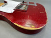 Close-up of a vintage red electric guitar body with worn, distressed finish and exposed wood, showing chrome bridge and control knobs against a gray background.
