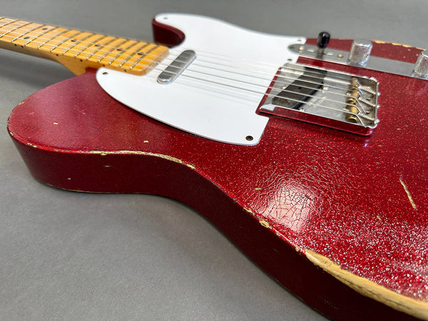 Close-up of red vintage electric guitar body with white pickguard and maple neck showing worn edges and textured finish on gray background