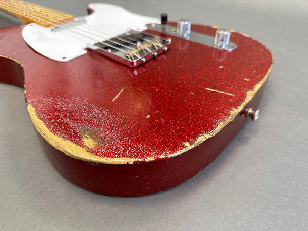 Close-up of worn red electric guitar body with visible paint chips and scratches on grey background