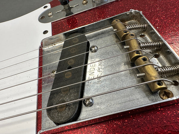 Close-up of the bridge and pickup on a red sparkle Fender electric guitar showing vintage metal parts and strings