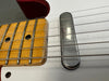 Close-up of electric guitar neck and metal pickup on white guitar body showing frets, strings, and worn maple fingerboard edge.