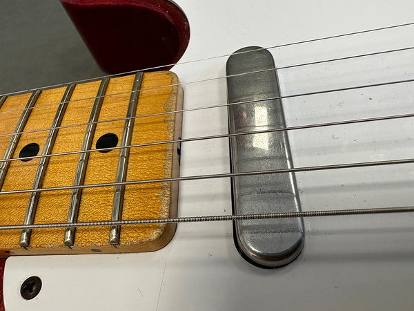 Close-up of electric guitar neck and metal pickup on white guitar body showing frets, strings, and worn maple fingerboard edge.