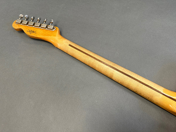 Back view of maple guitar neck with vintage-style tuning pegs and skunk stripe on a brown background
