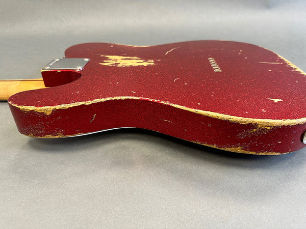 Close-up of vintage red electric guitar body with worn and chipped edges showing natural wood underneath on gray background
