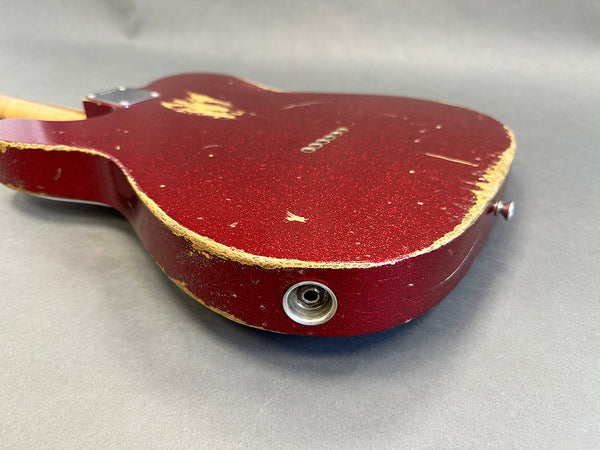Close-up of worn red electric guitar body with visible paint chips and input jack on gray background