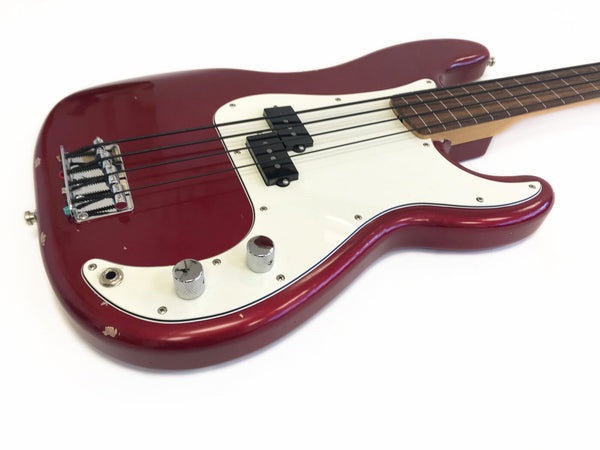 Close-up view of a red electric bass guitar with white pickguard, chrome knobs, and black pickups on a white background showing minor paint chips and wear.