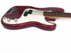 Close-up of red electric bass guitar body with white pickguard and chrome control knobs on white background